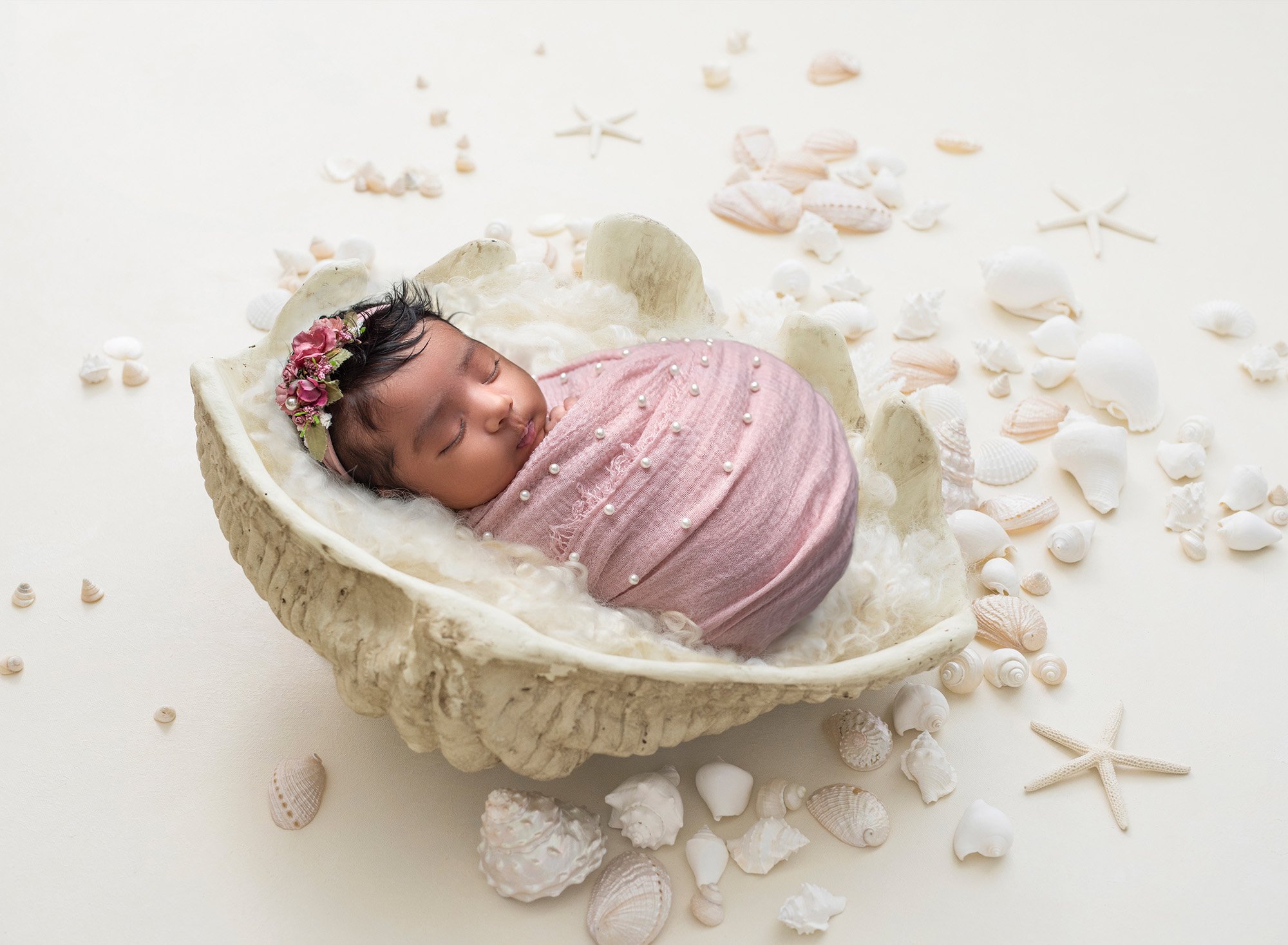 Newborn Girl Photography newborn baby girl swaddled in pink blanket of pearls sleeping inside large beach shell surrounded by miniature shells and starfish