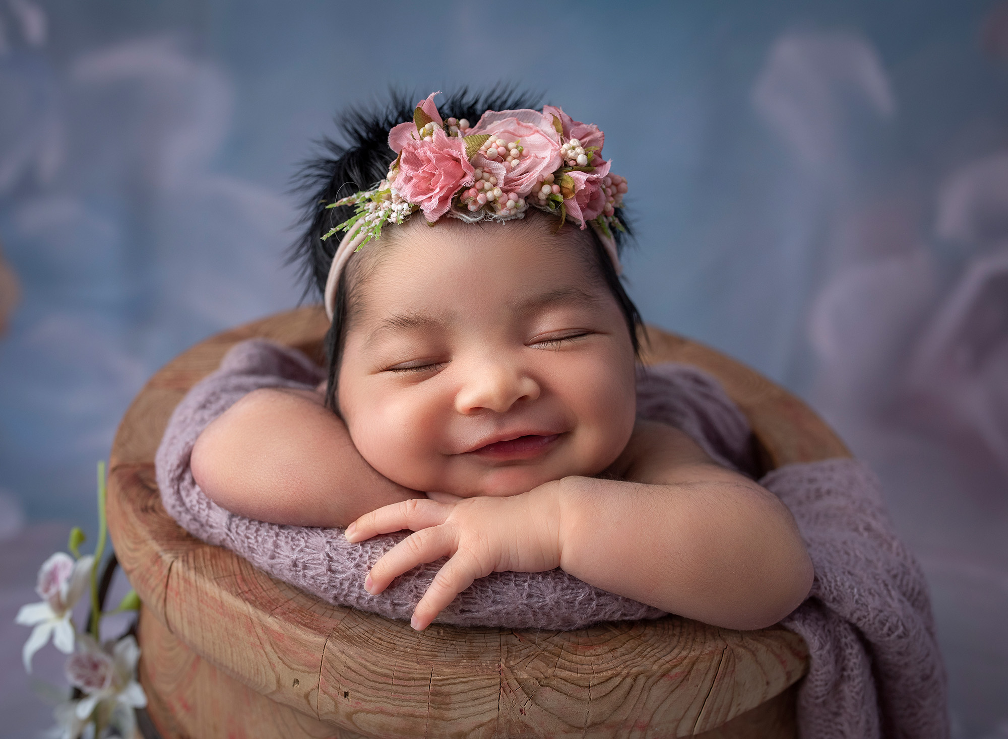 newborn baby girl happily smiling while asleep in honey pot wearing pink headband