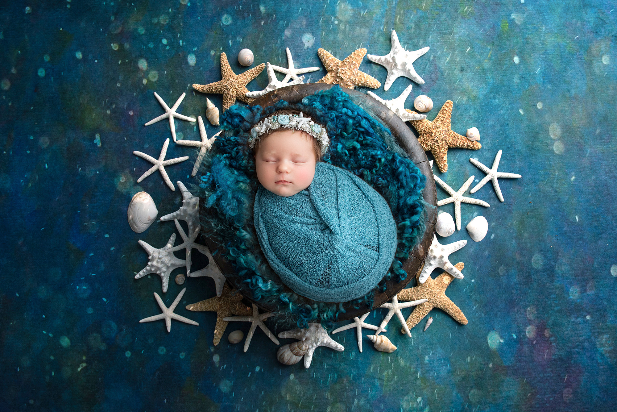 newborn baby girl asleep in rustic bowl swaddled in teal surrounded by starfish and shells