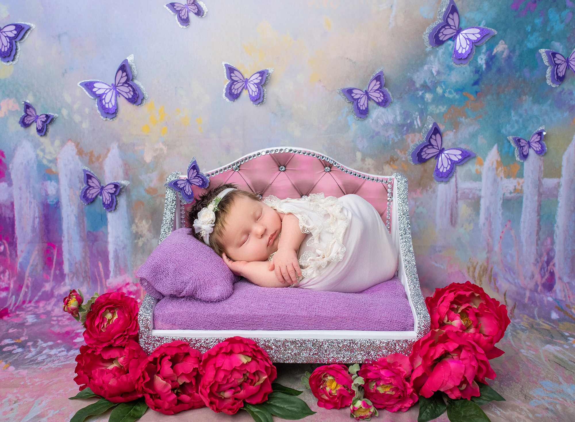 Newborn Photos with Butterflies newborn baby girl sound asleep on glittered miniature bed covered in purple surrounded by pink flowers and butterflies