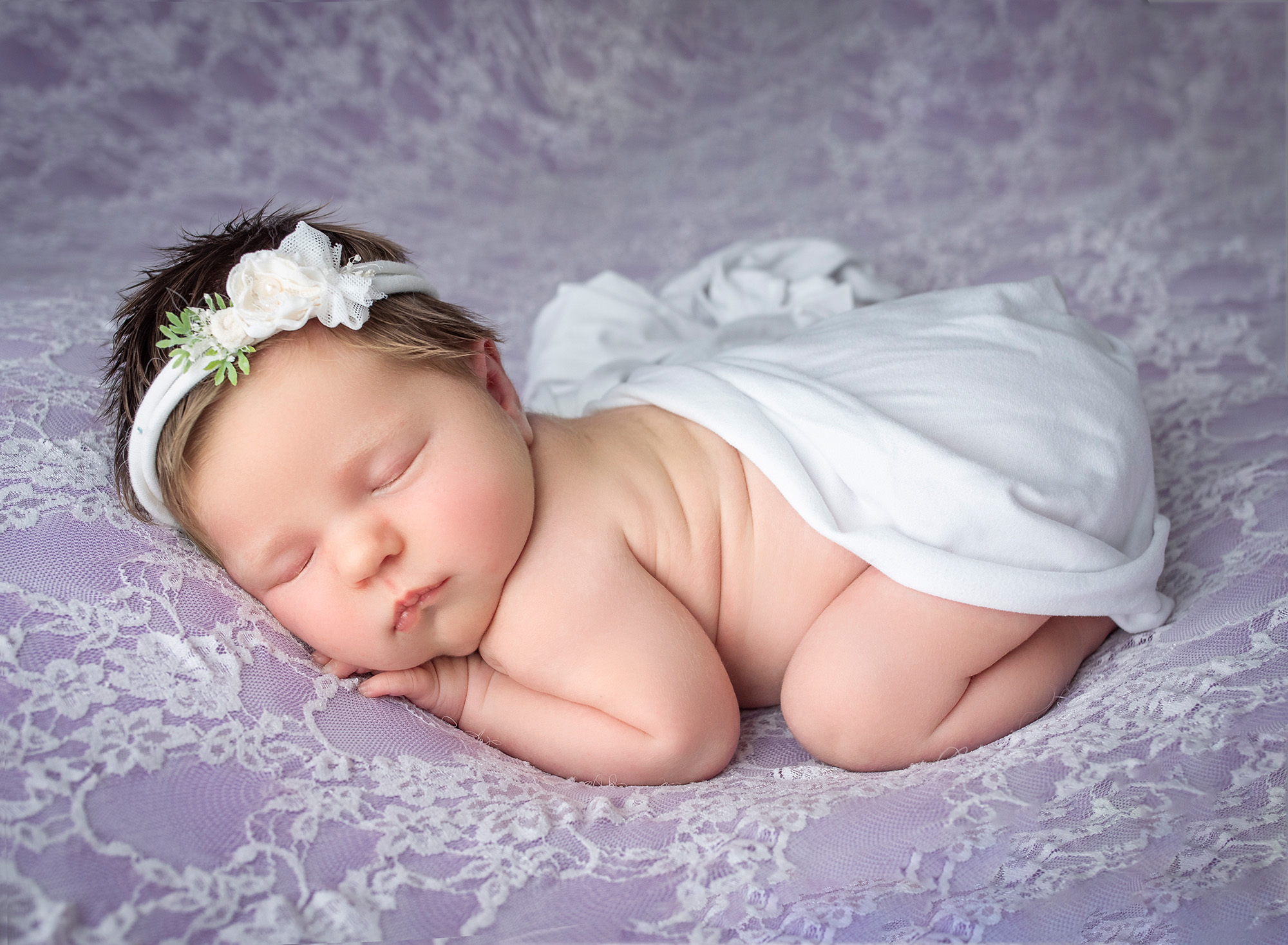 newborn baby girl asleep on purple laced blanket wearing white headband and wrap