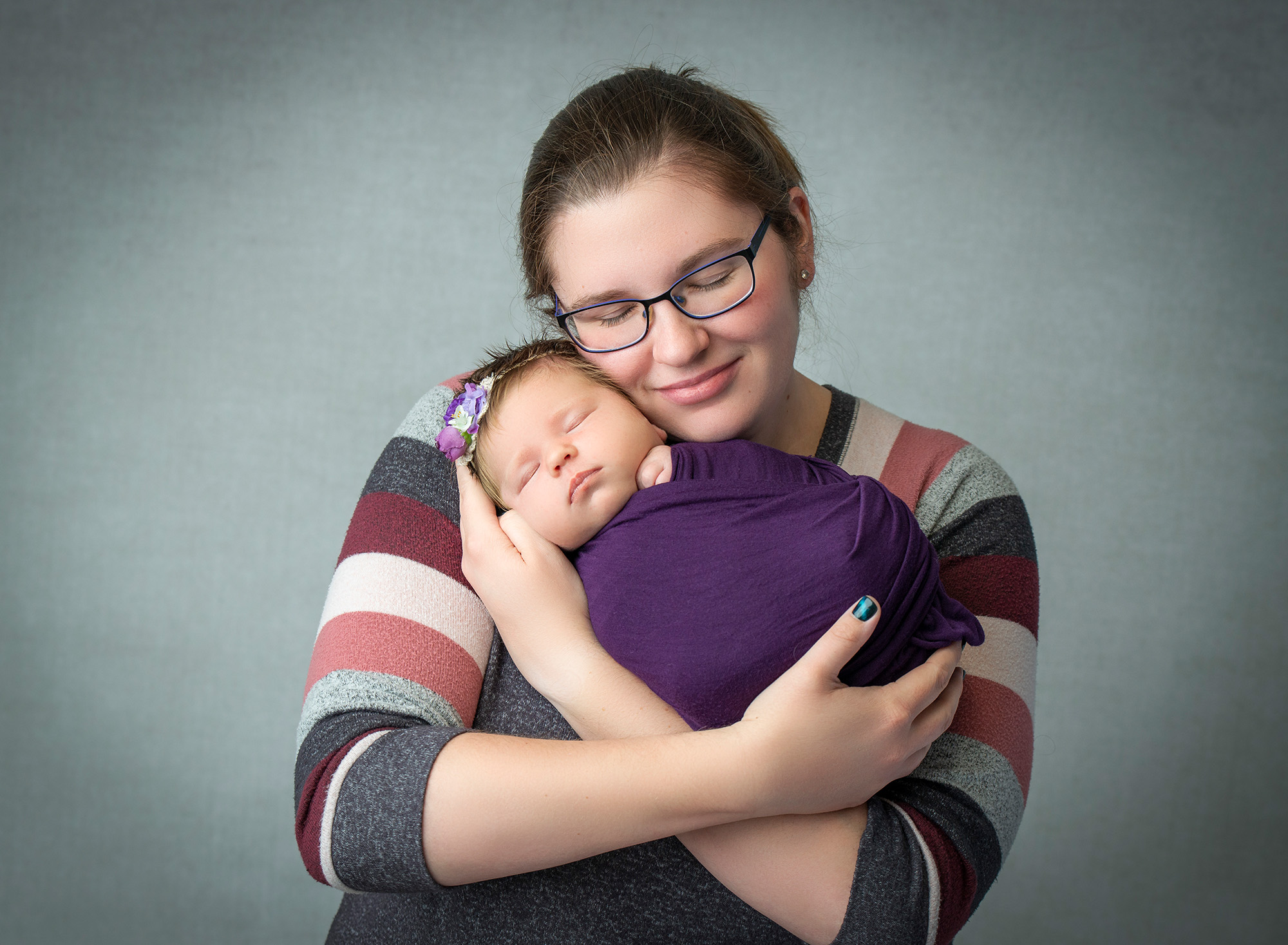 mom cradling newborn baby girl swaddled in purple
