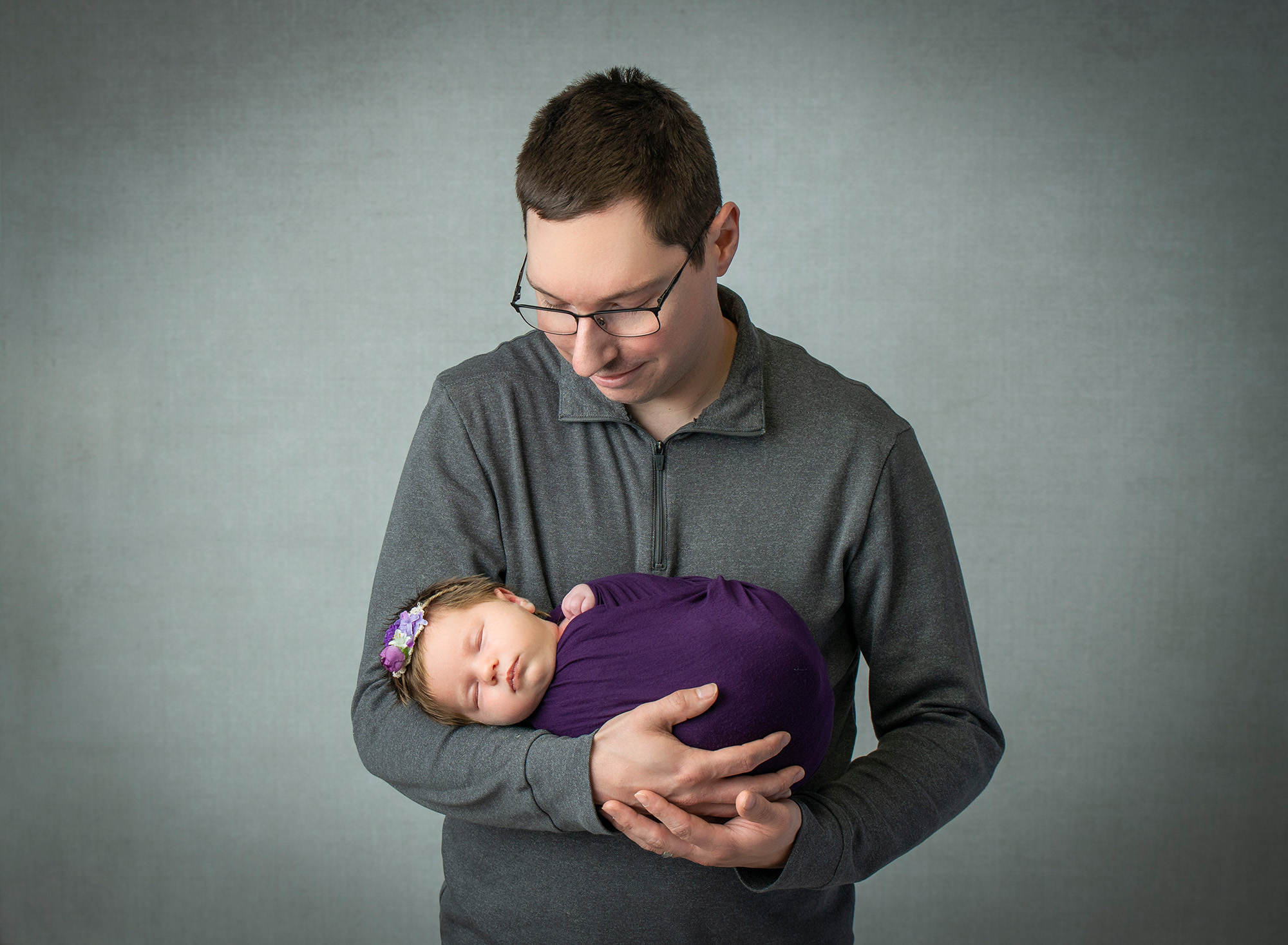 dad sweetly looking down on sleeping newborn baby girl swaddled in purple