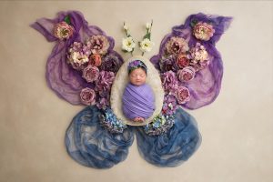 sweet newborn baby girl asleep swaddled in purple inside of a butterfly