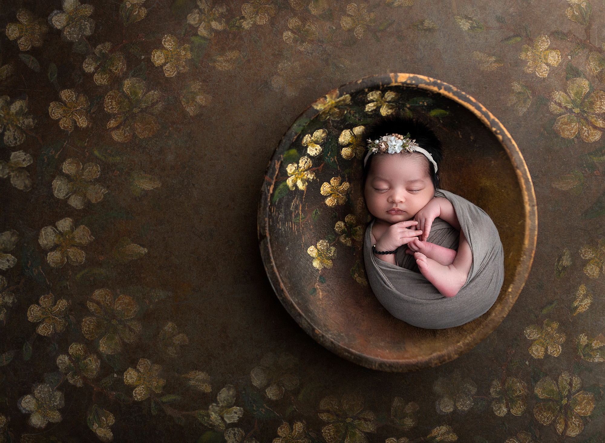newborn baby girl asleep in rustic bowl surrounded by golden flowers