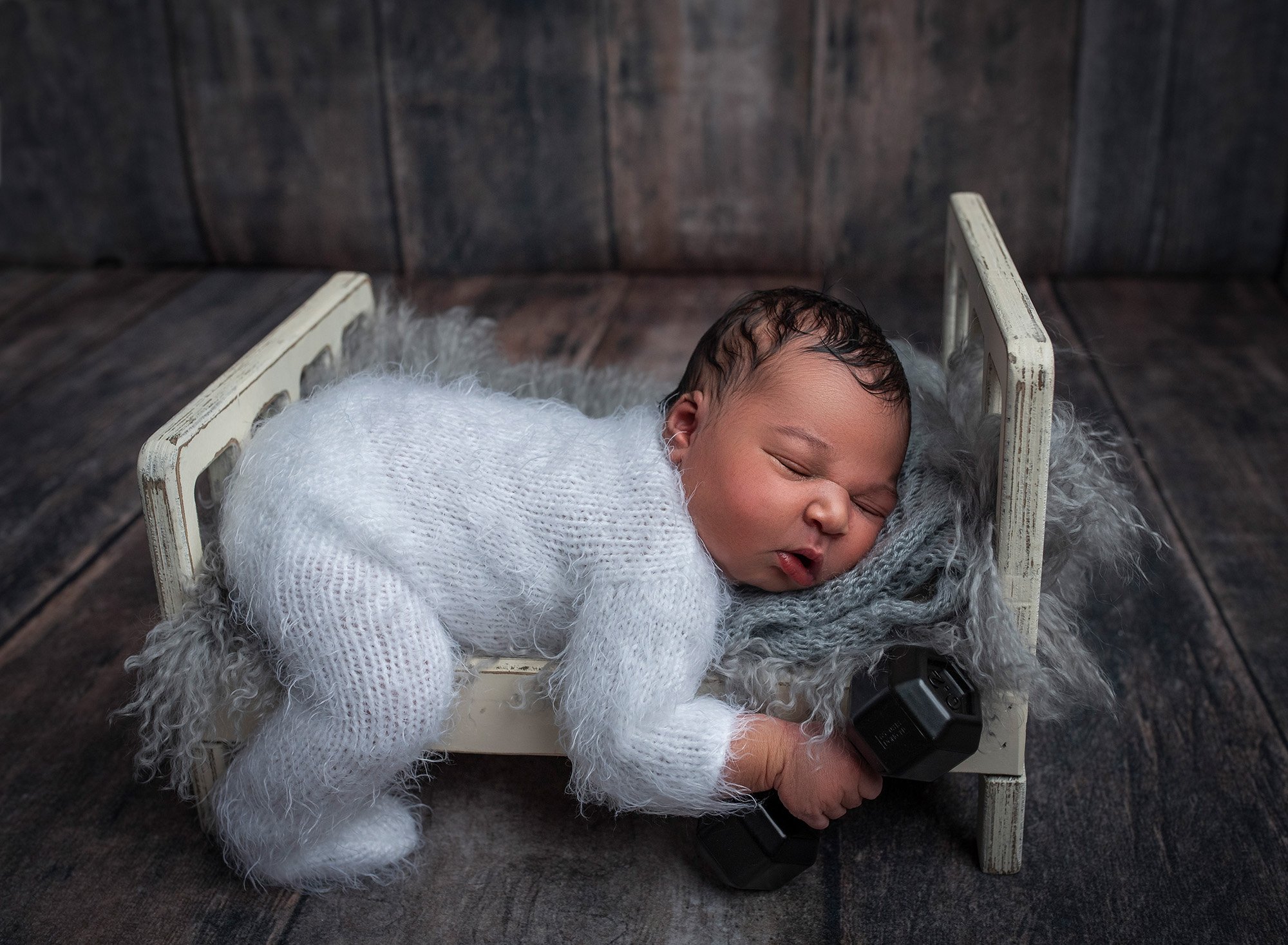 newborn baby boy asleep on a rustic bed holding a weight