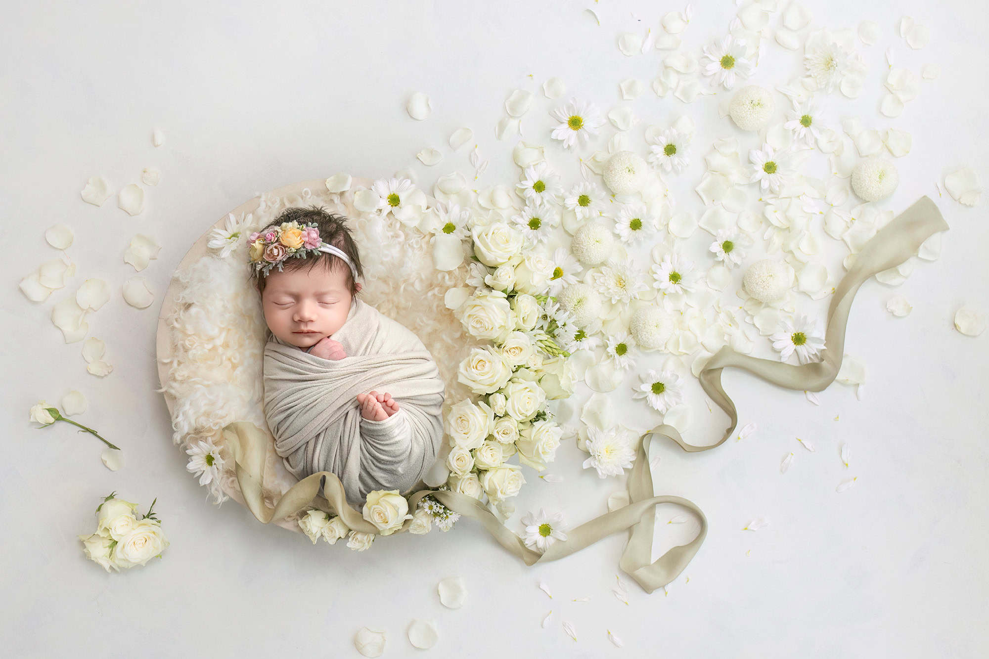 CT newborn photographer swaddled baby sleeping in a bowl surrounded by white flowers and a trailing beige ribbon