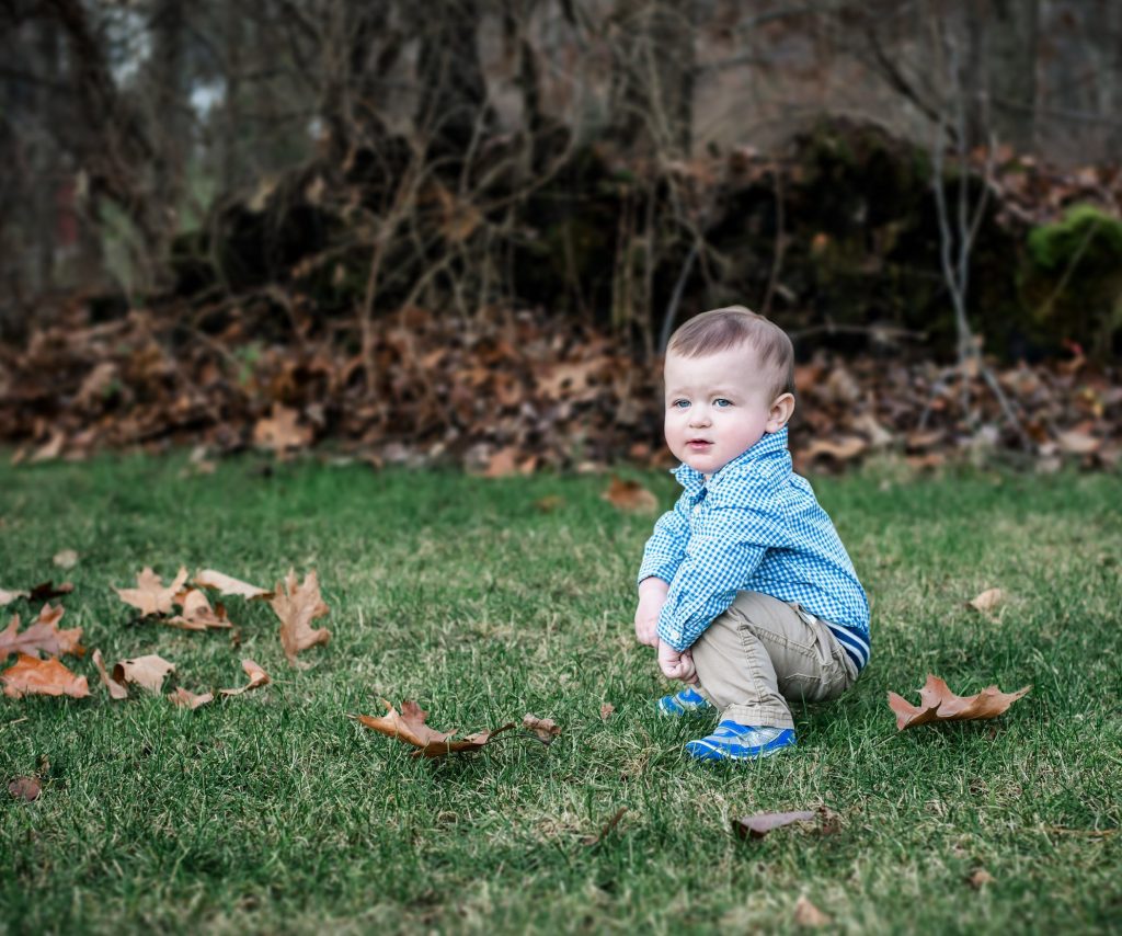 one-year-old boy squats down in the backyard in Fall to take a rest