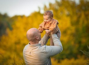 father holding up daughter in the air in a sunset setting