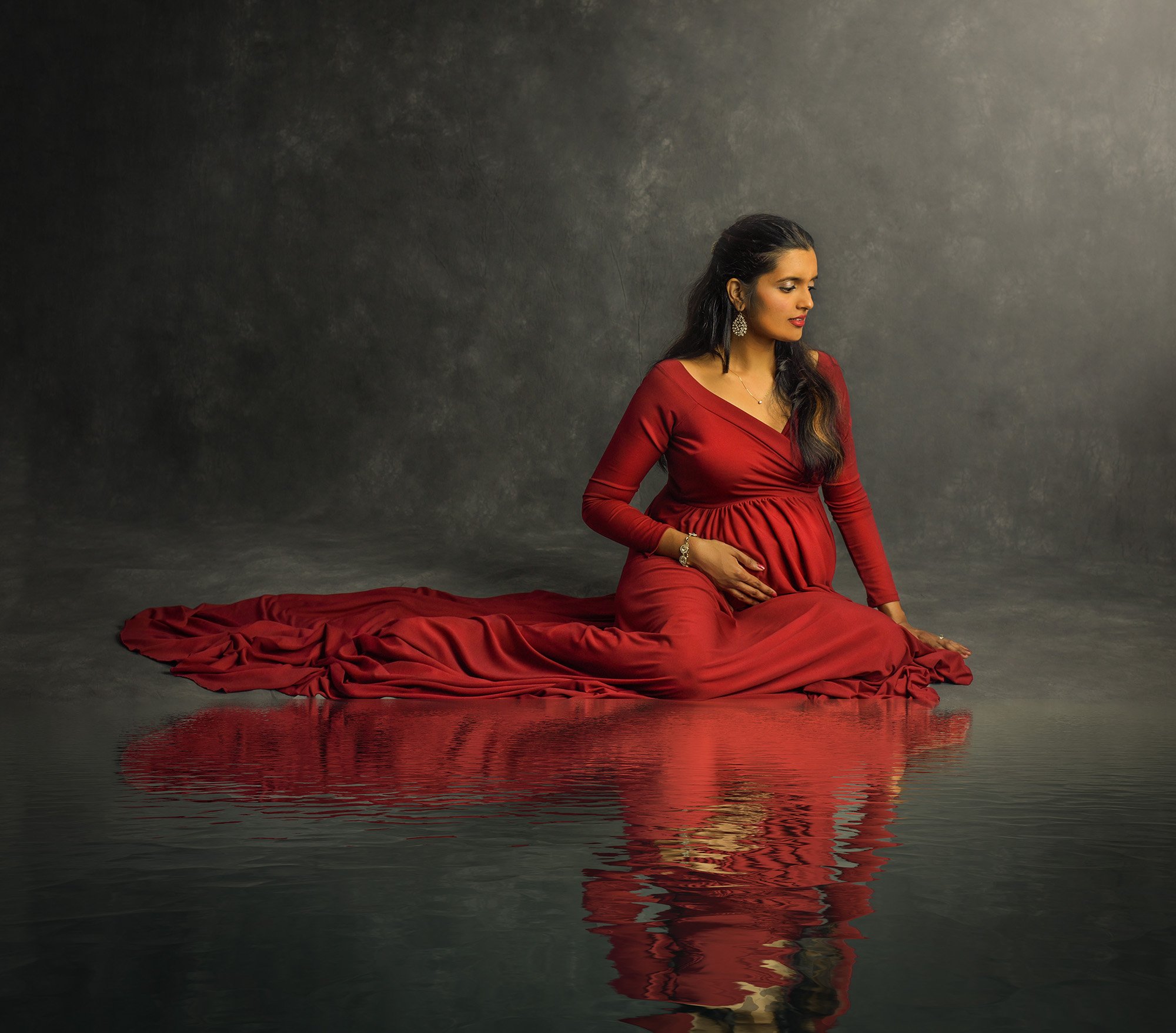 Professional Maternity Newborn Photographer pregnant woman wearing red maternity dress sitting on shadowed water