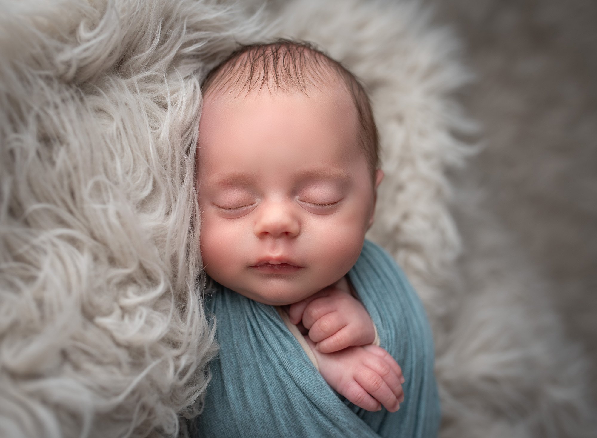 newborn baby boy wrapped in blue asleep on fluffy blanket