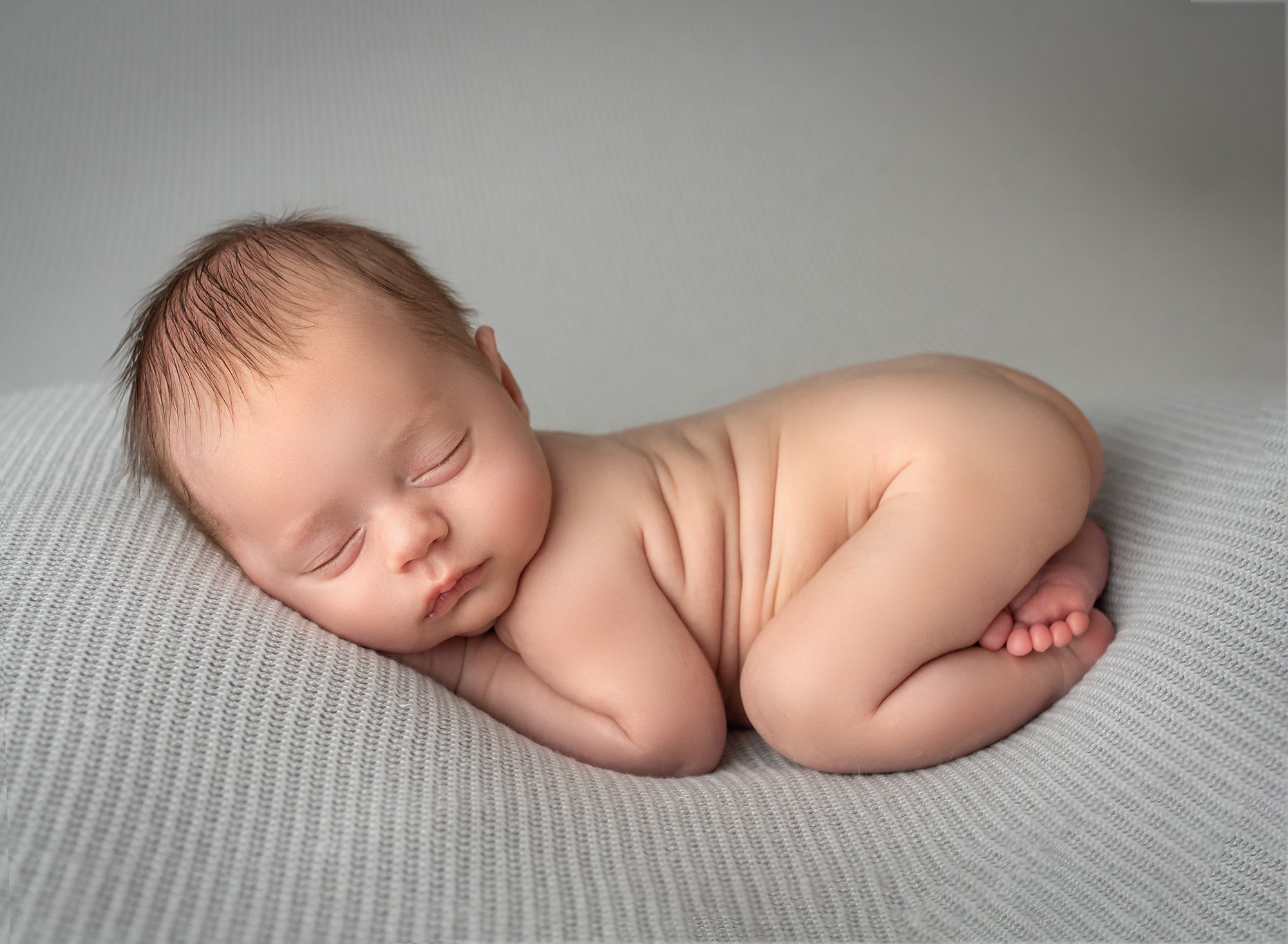 newborn baby boy sound asleep naked on white blanket with grey background