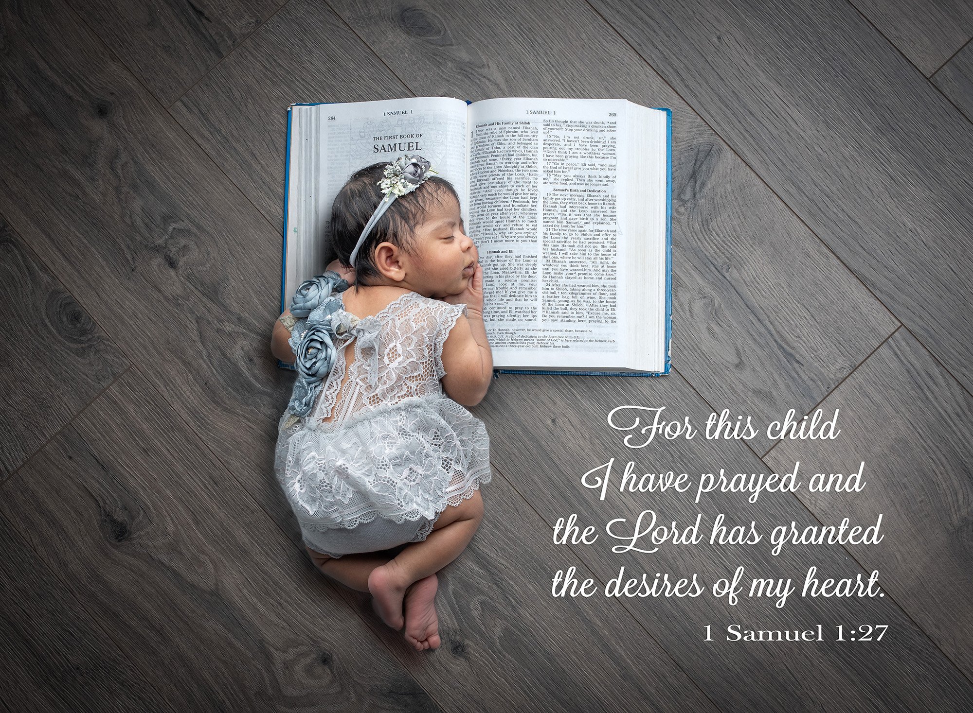 newborn photographs of an answered prayer newborn baby girl dressed in floral lace grey dress sound asleep with her head on the Bible including bible quote on wooden background