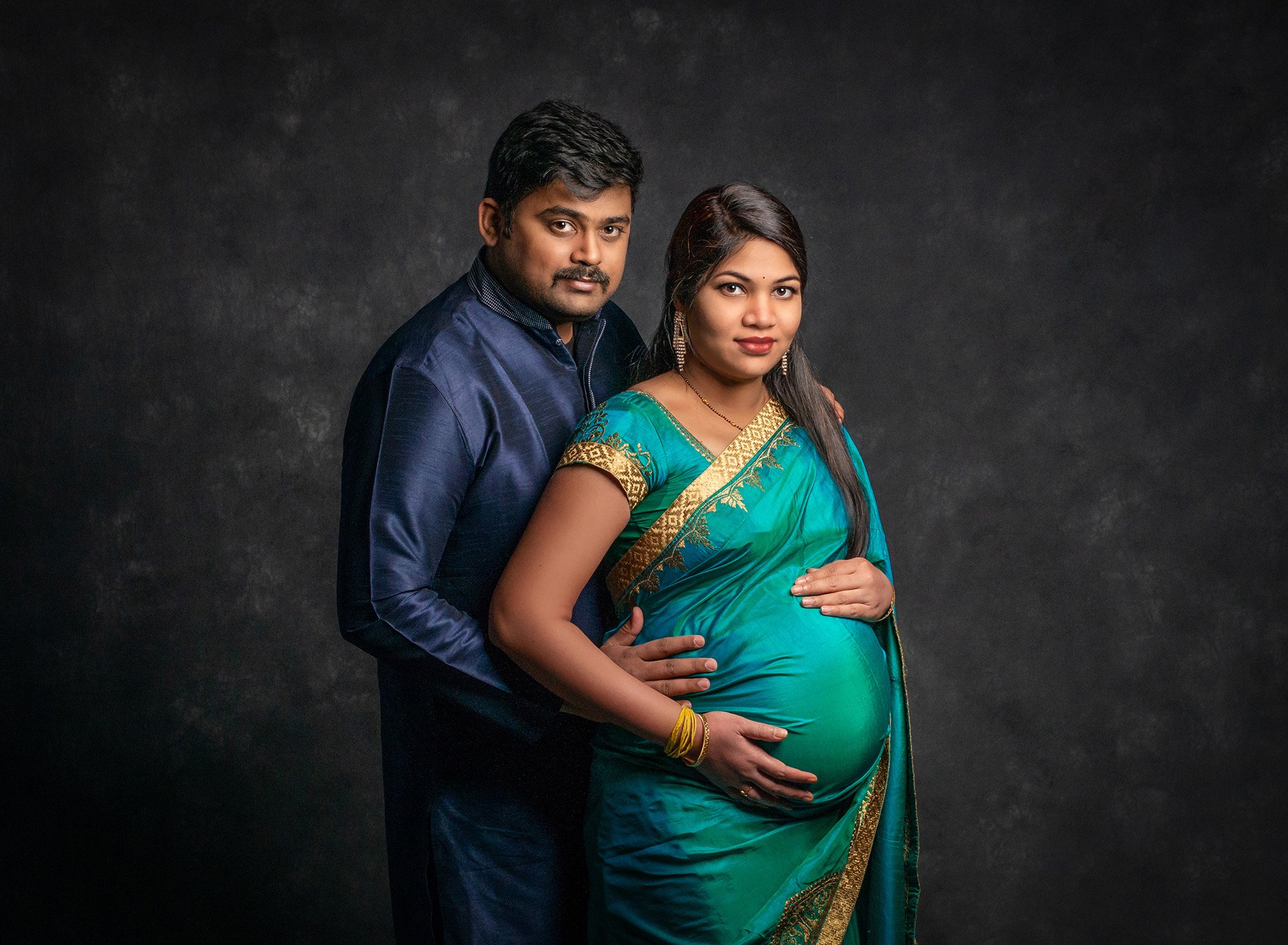 traditional Indian clothes maternity photo pregnant woman posing with husband in Indian dress clothing on gray backdrop