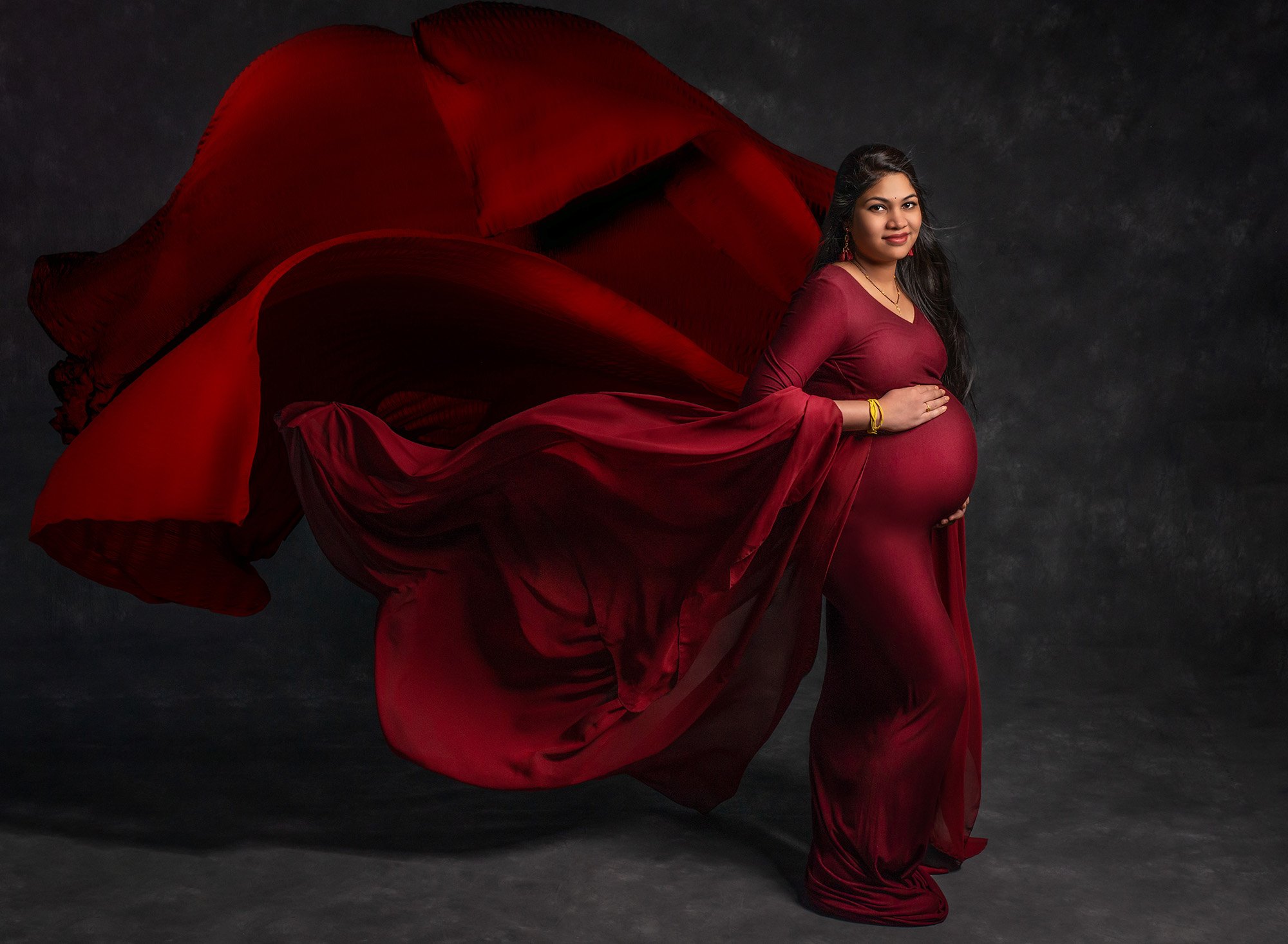 flowing cranberry maternity dress on dark gray backdrop