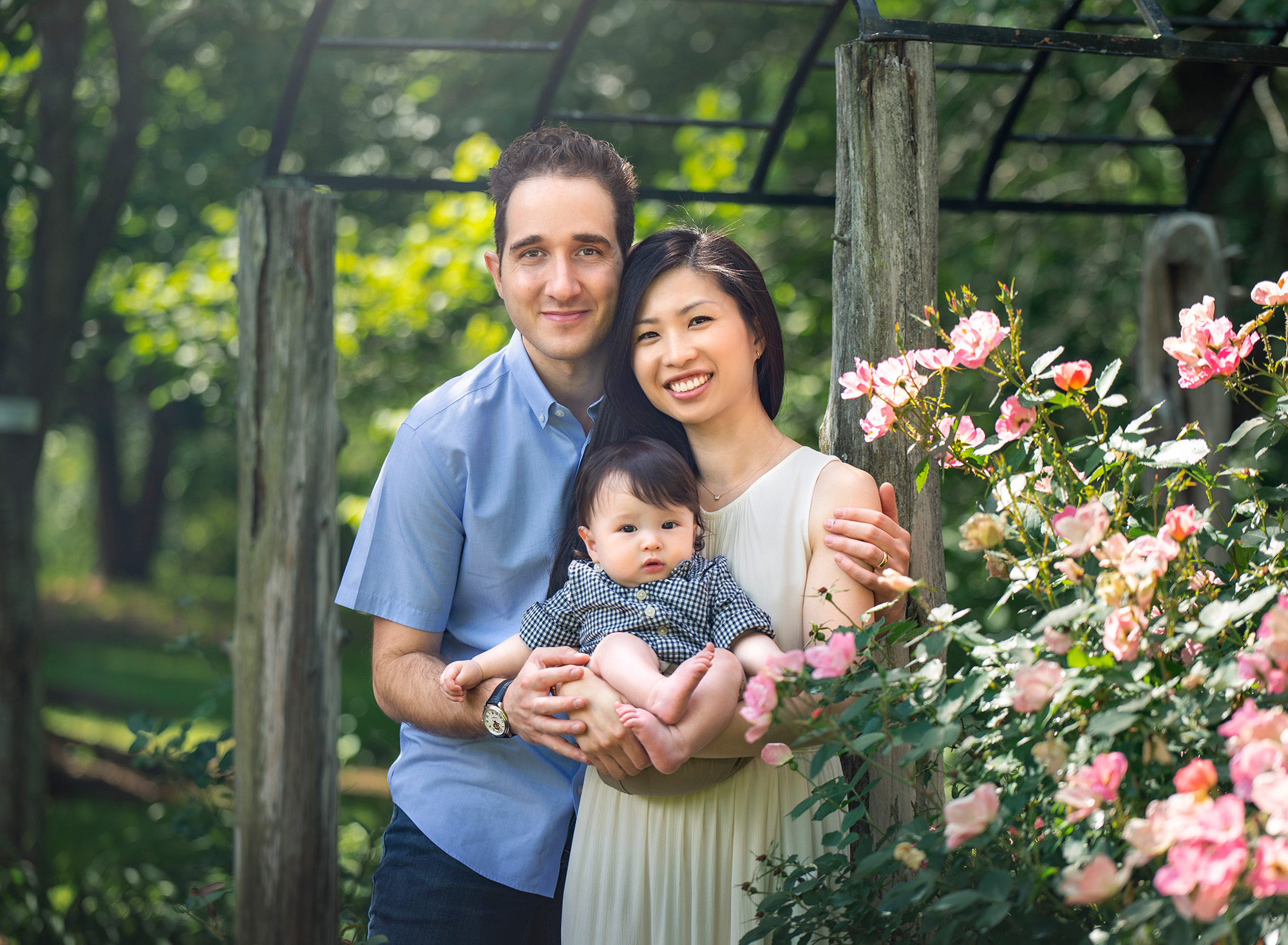 connecticut baby photographer couple posing with toddler son outside next to a pink flower bush