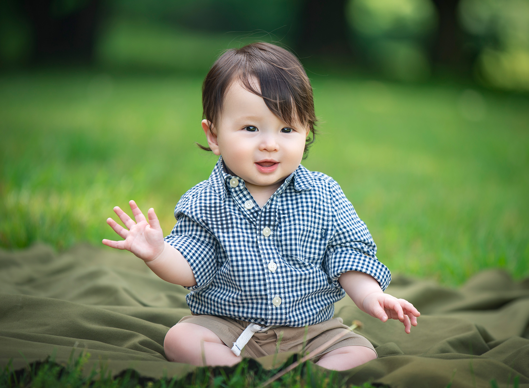 Connecticut Baby Photographer toddler in black and white checkered button up smiling while sitting on blanket in the grass