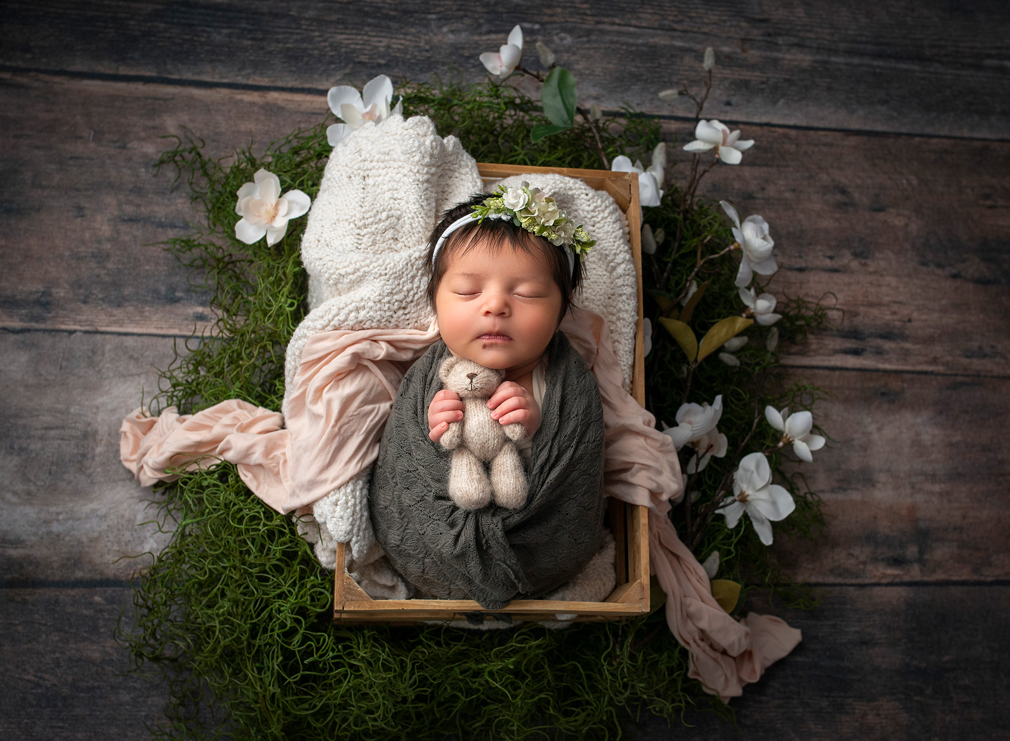 outdoorsy newborn photos newborn baby girl asleep in box surrounded by moss and white flowers holding felt teddy bear