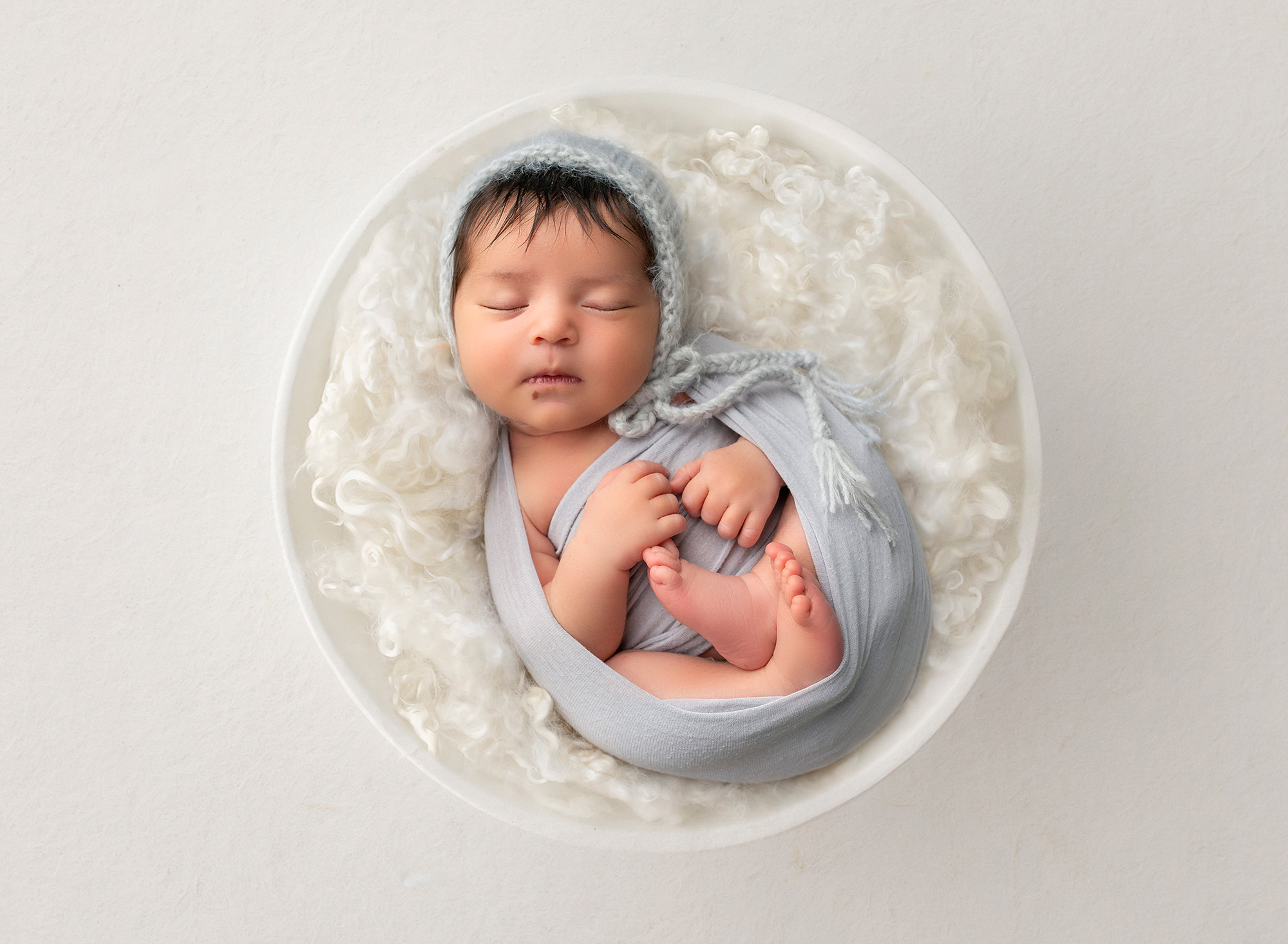 newborn baby girl swaddled in gray laying on top of fluffy blanket in bowl