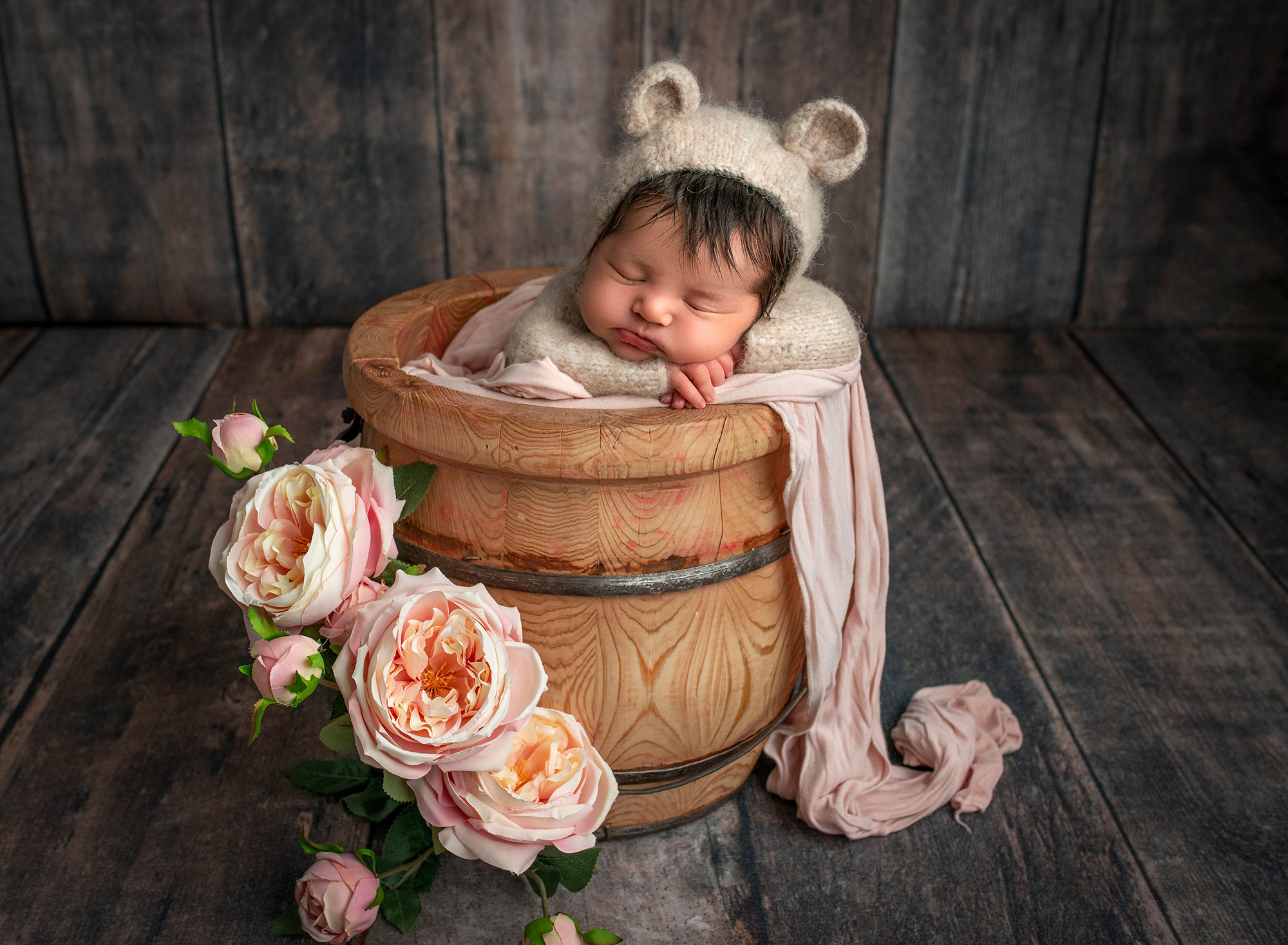 newborn baby girl asleep wearing bear romper inside of honey pot surrounded by pink flowers