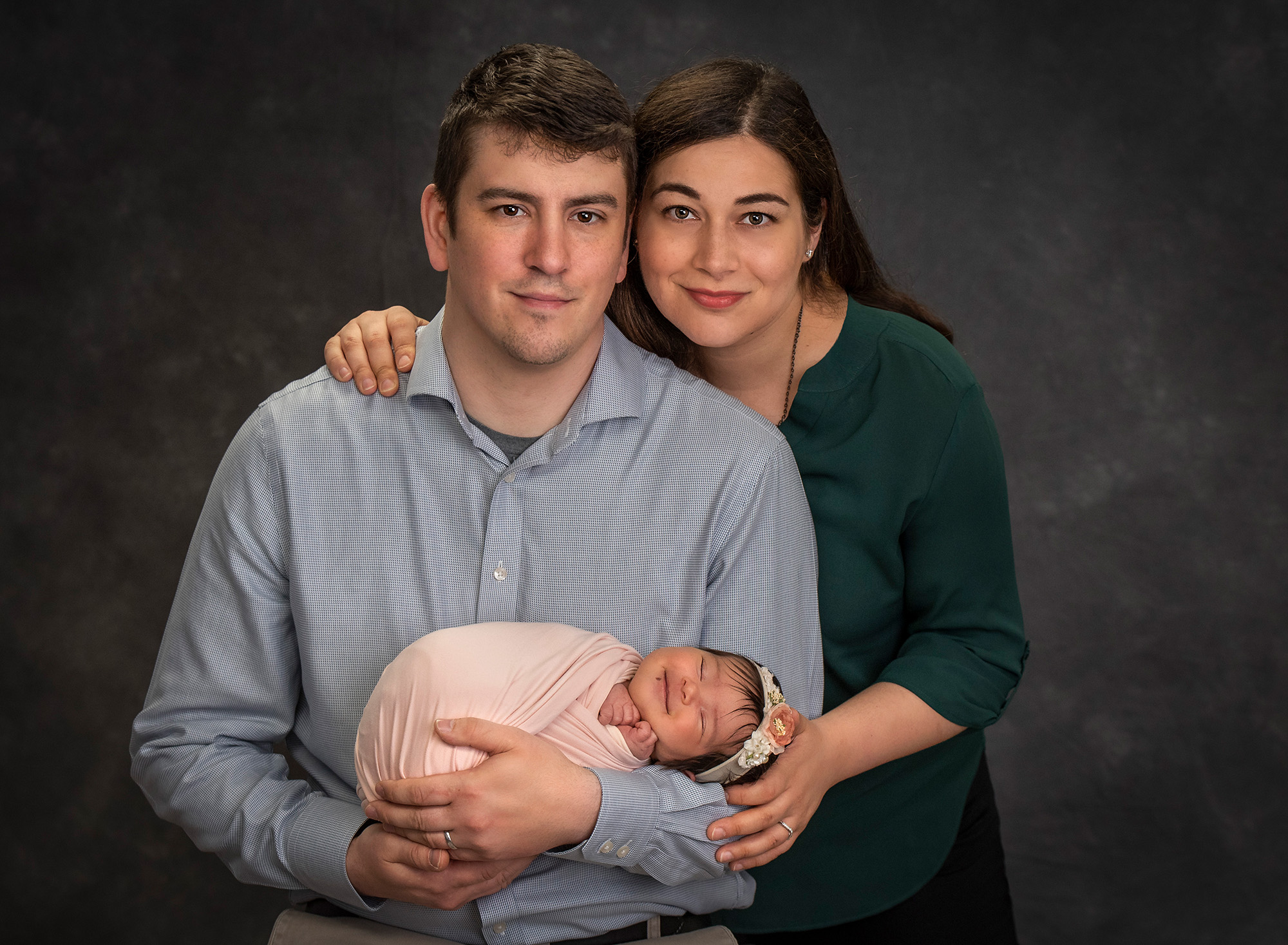 couple posing while cradling newborn baby girl swaddled in light pink