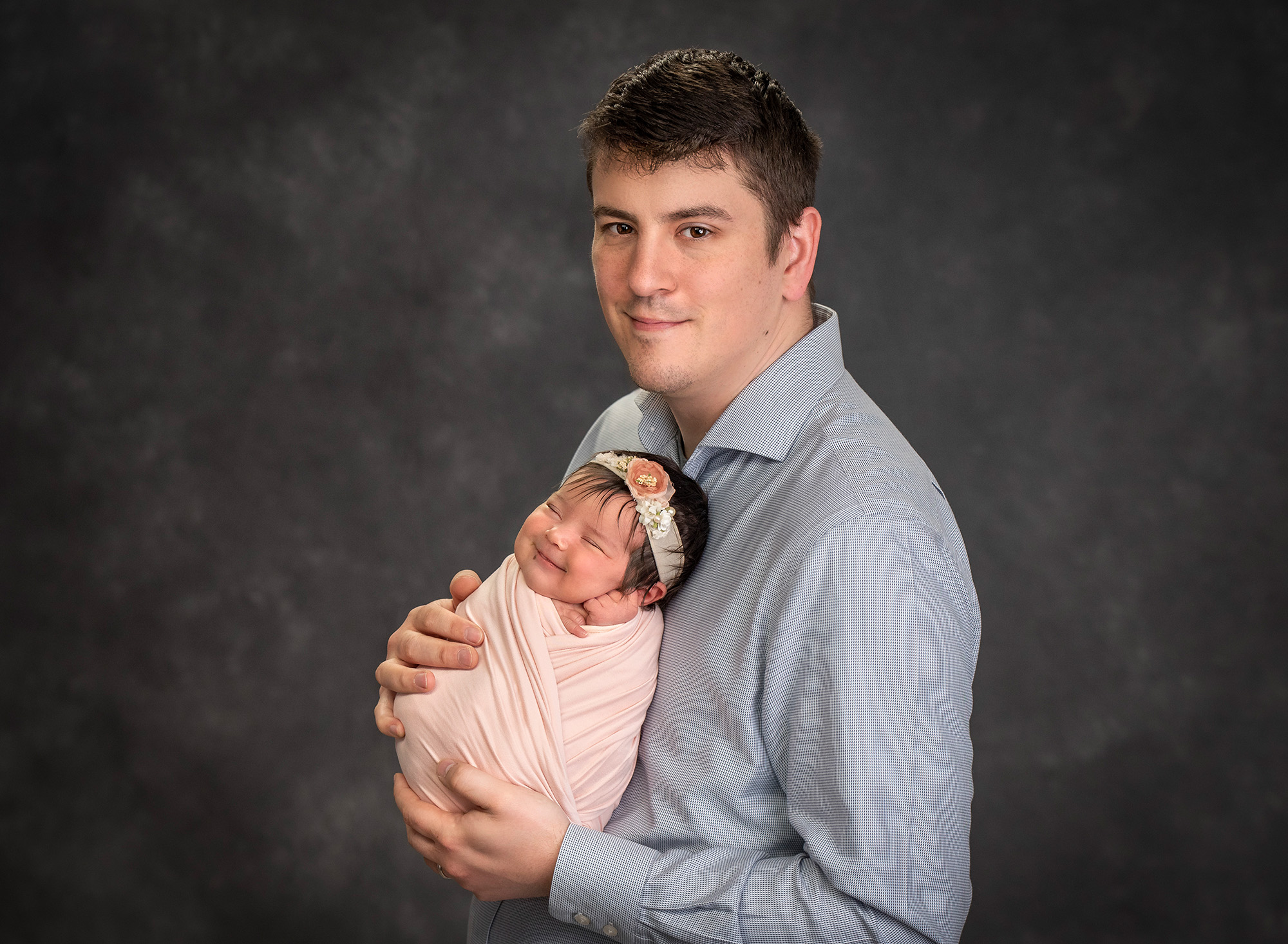 newborn photographer in CT new dad cradling newborn baby girl swaddled in light pink