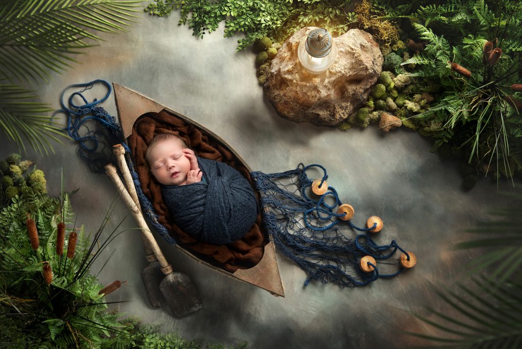 newborn baby boy asleep in a row boat floating down the river
