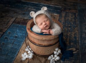 newborn baby boy asleep in bear romper inside honey pot